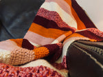 Load image into Gallery viewer, crochet blanket with stripes of orange, burgundy, pink, and white draped over leather chair

