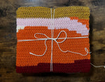 Load image into Gallery viewer, Folded crochet blanket with uneven stripes of orange, burgundy, pink, and gold.
