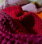 Load image into Gallery viewer, Close up photo of crochet blanket showing showing stripes of burgundy, red, orange, pink, gold, and white.
