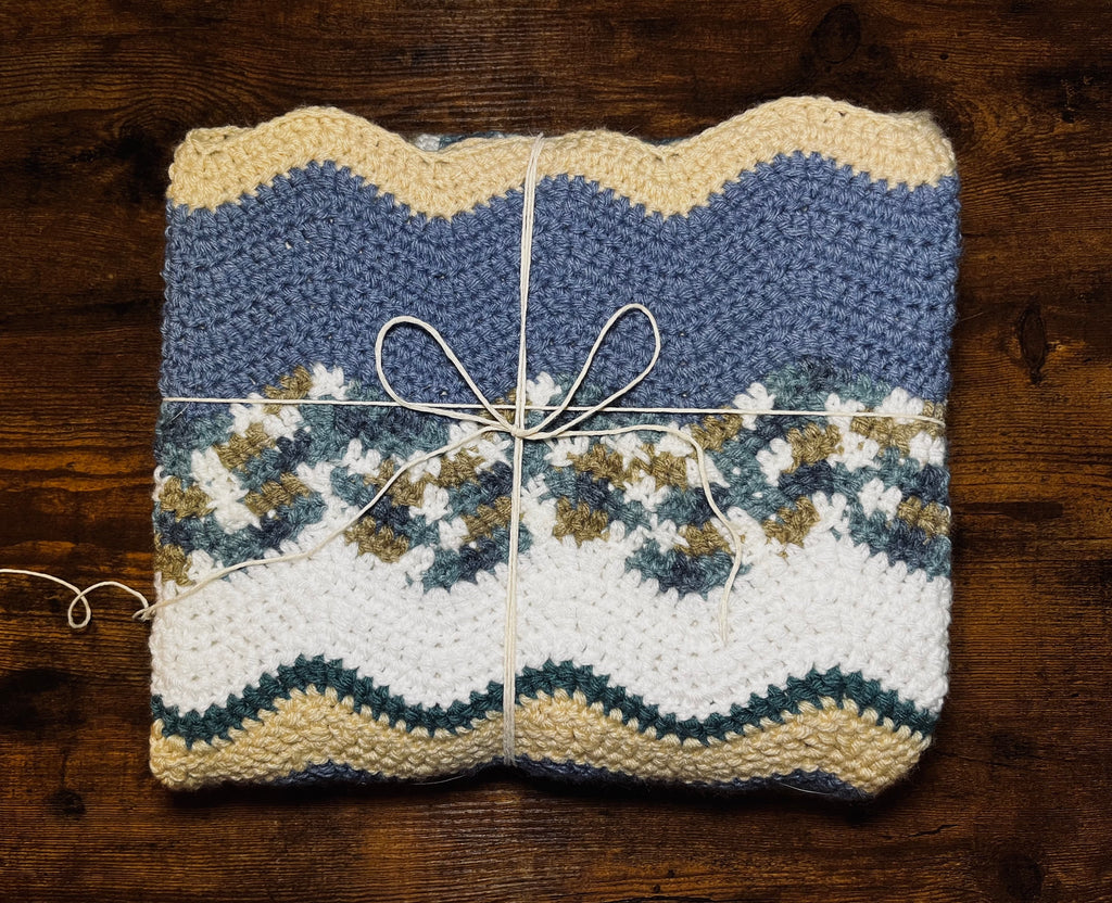 Folded crochet blanket in wavy stripes of white, beige, turquoise, light blue, and brown.