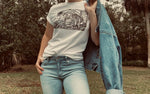 Load image into Gallery viewer, White t-shirt with black abstract wave print on model wearing blue jeans and holding a jean jacket

