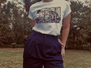 White t-shirt with black abstract wave print on model wearing navy blue high waisted trousers